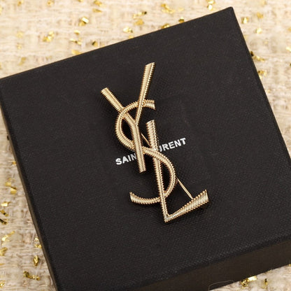 Gold YSL brooch on a black Saint Laurent box with gold confetti background